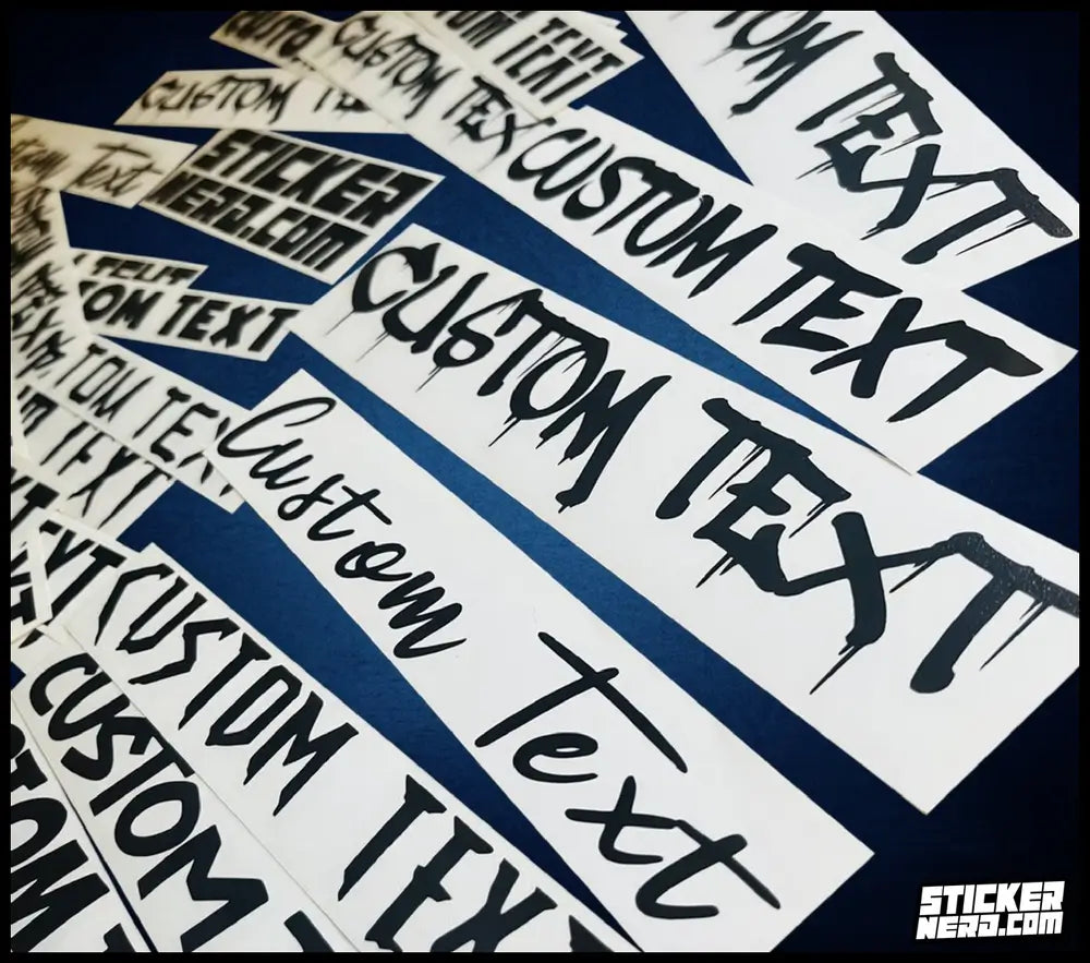 A pile of white rectangular stickers with black custom text reading 'CUSTOM TEXT' and 'STICKERNERD.COM' printed on them, arranged diagonally on a dark navy background.