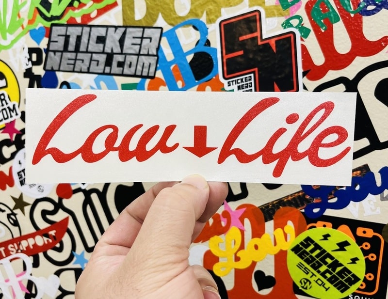 Sticker with 'Low Life' text held over a colorful background of other stickers.