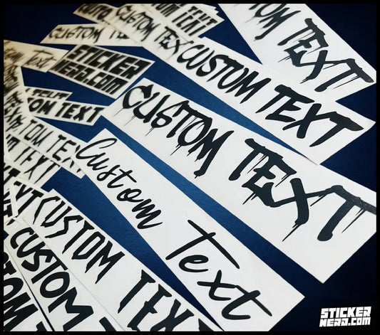 A pile of white rectangular stickers with black custom text reading 'CUSTOM TEXT' and 'STICKERNERD.COM' printed on them, arranged diagonally on a dark navy background.