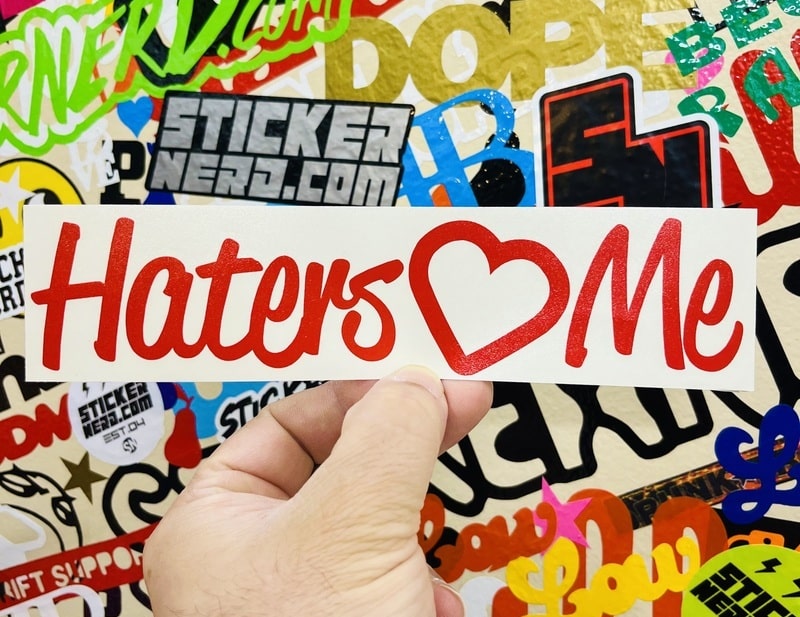 Sticker with 'Haters Love Me' text held over a colorful background of other stickers.