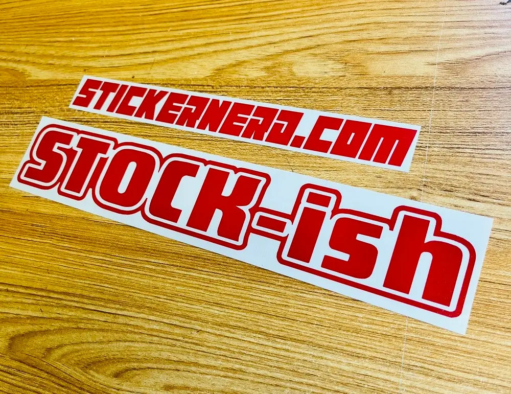 Two red and white vinyl stickers on a light brown wood grain surface. The top sticker reads 'STICKERNERD.